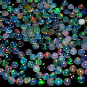 May include: A collection of round, iridescent opal gemstones in various shades of blue, green, and red. The opals are arranged in a random pattern on a black background.