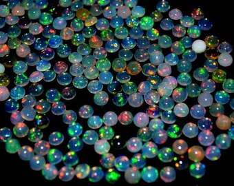 May include: A scattering of small, round opals with a polished, iridescent finish. The opals exhibit a range of colours, including blue, green, orange, and red, set against a dark backdrop. The gemstones are spread out, creating a visually attractive arrangement.