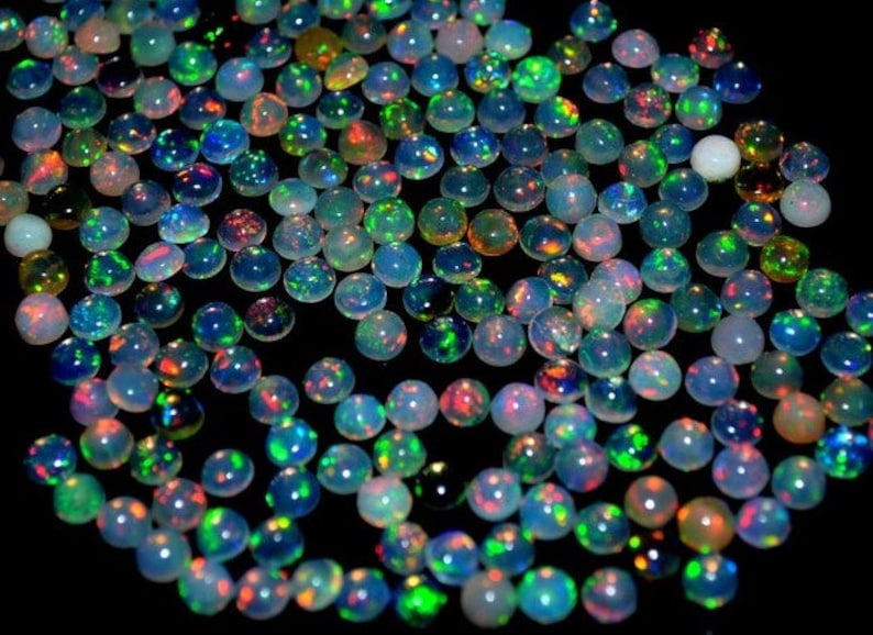 May include: A collection of round, iridescent opal gemstones in various shades of blue, green, and red. The opals are arranged in a random pattern on a black background.