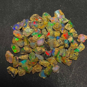 May include: A collection of rough opal gemstones, displaying a variety of colors including green, red, blue, and yellow. The opals have a rough, natural texture and are set against a dark background.