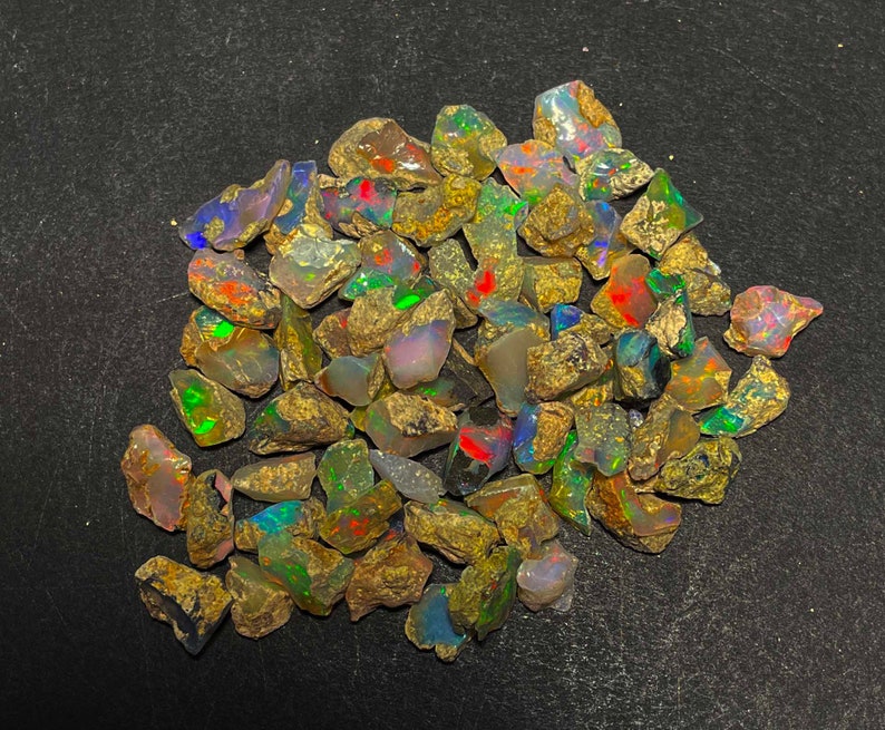 May include: A collection of rough opal gemstones, displaying a variety of colors including green, red, blue, and yellow. The opals have a rough, natural texture and are set against a dark background.