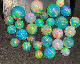 May include: A collection of 25 iridescent opal cabochons in various sizes and shades of blue, green, and white. The opals have a rainbow sheen and are perfect for jewellery making.