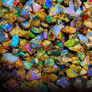 May include: A close-up view of a pile of rough opal gemstones. The opals display a variety of colors, including blue, green, red, and yellow, with a shimmering, iridescent effect. The opals are surrounded by a matrix of brown rock.