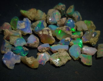 Puede incluir: Una colección de piedras de ópalo en bruto de varios colores, incluyendo blanco, azul, verde y rosa. Las piedras son iridiscentes y tienen un aspecto natural y en bruto.