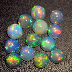 May include: A collection of round, iridescent opal gemstones. The opals are various shades of white, blue, green, and red. The opals are smooth and polished.