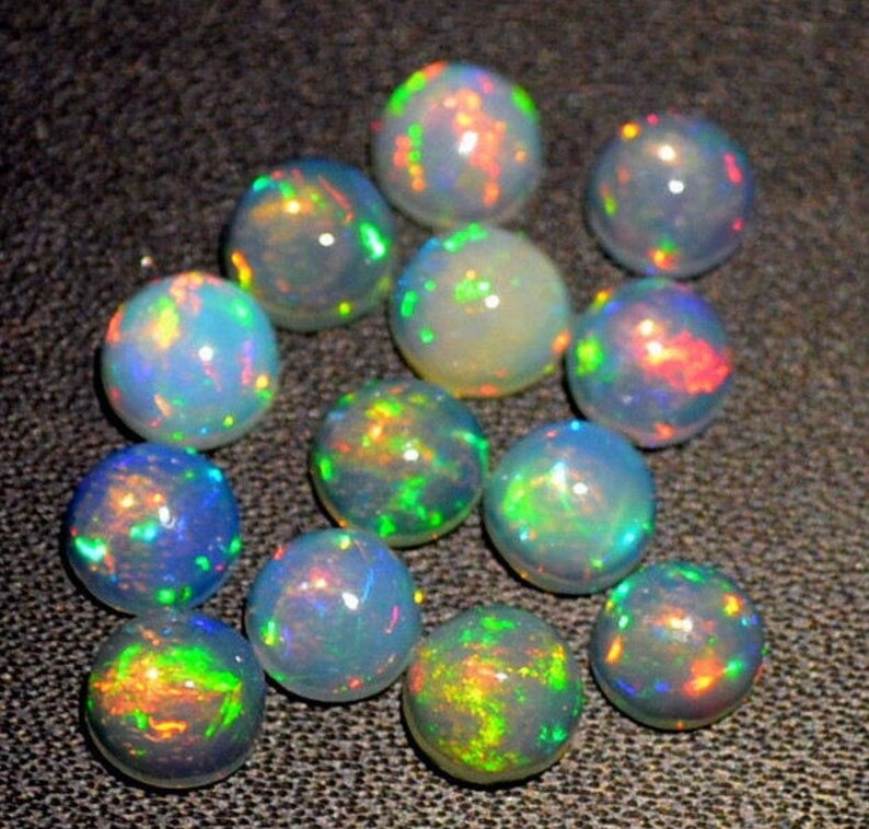 May include: A collection of round, iridescent opal gemstones. The opals are various shades of white, blue, green, and red. The opals are smooth and polished.