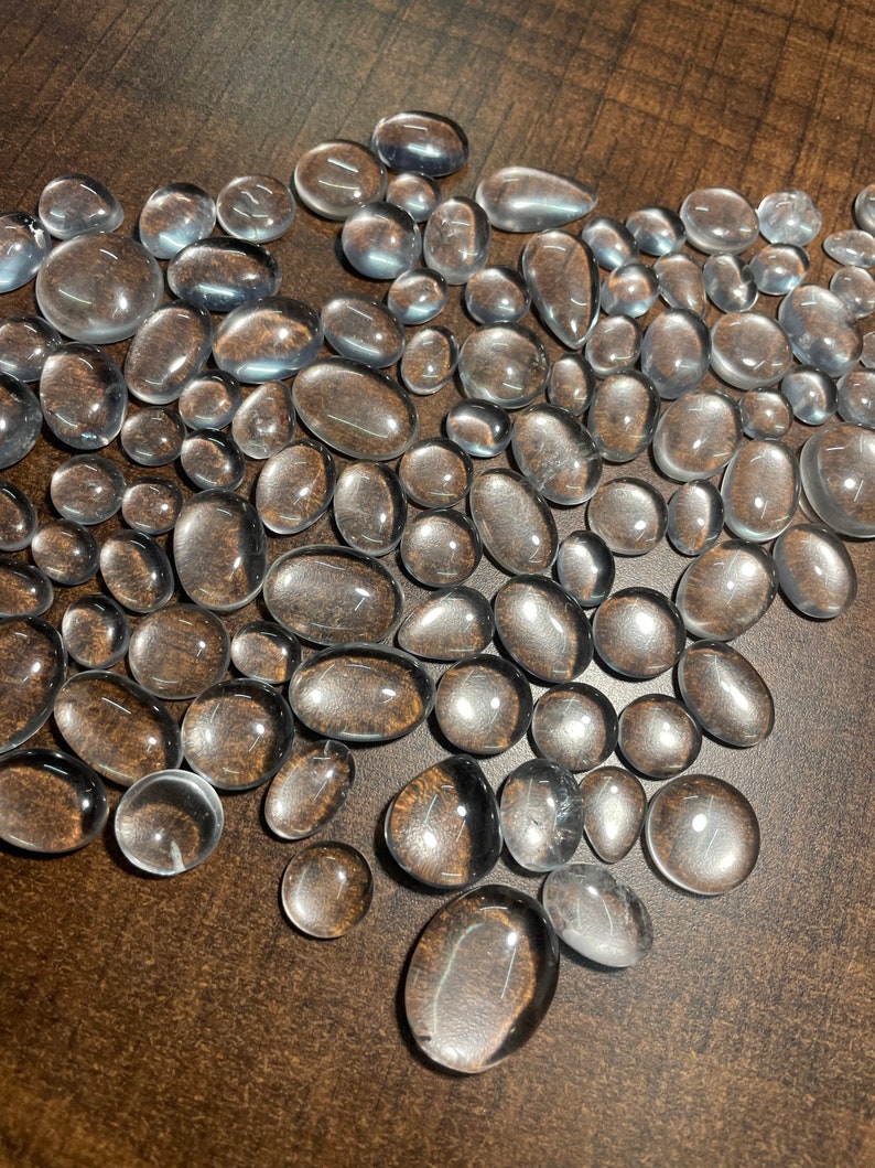 May include: A large group of clear, smooth, oval-shaped stones. The stones are scattered on a brown surface.