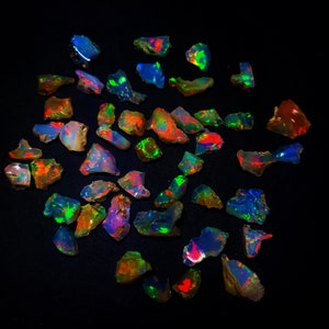 May include: A collection of iridescent opal gemstones in various shapes and sizes. The opals display a rainbow of colours, including red, green, blue, and purple.