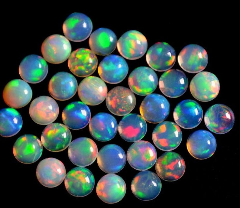 May include: A collection of round, iridescent opal cabochons in various shades of blue, green, and pink. The opals are smooth and polished, with a high luster.