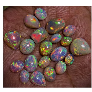 Könnte beinhalten: Eine Sammlung von 18 regenbogenfarbenen Opal-Edelsteinen in verschiedenen Formen und Größen. Die Opale sind eine Mischung aus hell- und dunkelgrau mit Schimmern in Grün, Blau, Rot und Gelb.