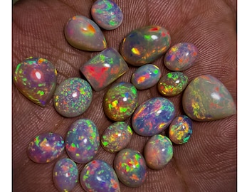 May include: A collection of 18 iridescent opal gemstones in various shapes and sizes. The opals are a mix of light and dark grey with flashes of green, blue, red, and yellow.