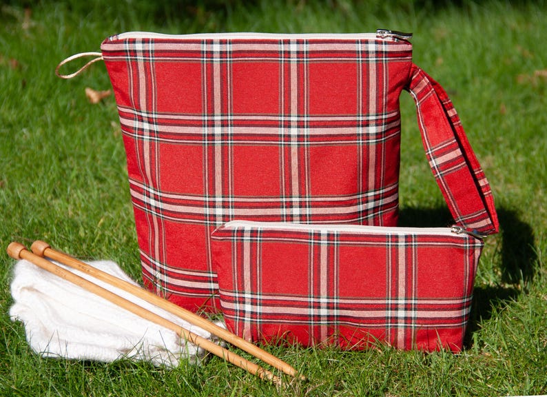 May include: Two red and white plaid zippered pouches with a white yarn ball and wooden knitting needles on a green grassy surface.