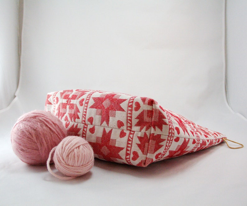 May include: A white and red patterned fabric tote bag with two pink yarn balls in front of it.