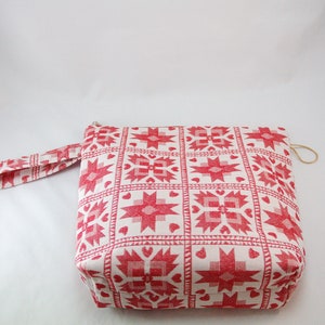 May include: A white zippered pouch with a red and white geometric pattern. The pouch has a red fabric handle.