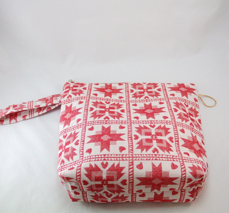 May include: A white zippered pouch with a red and white geometric pattern. The pouch has a red fabric handle.