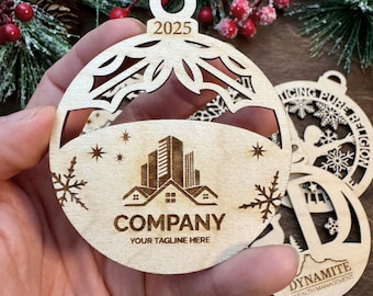May include: Wooden Christmas ornament with a cut-out design, featuring a company logo, snowflakes, and the year 2025. The ornament is round with a hole at the top for hanging. Additional ornaments are visible in the background.