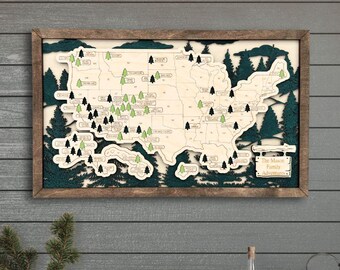 May include: A wooden map of the United States with a dark green frame. The map features a light-colored background with dark green and black trees marking locations. The text "The Mason Family Adventure" is visible on the map.