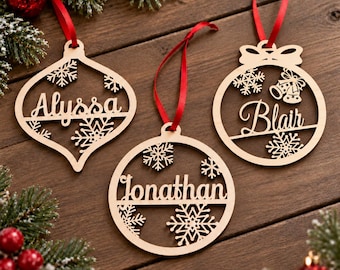 May include: Three laser-cut wooden Christmas ornaments with red ribbons. One teardrop-shaped ornament reads Alyssa, one circular ornament reads Jonathan, and one circular ornament with a bow detail reads Blair. Each features snowflake cutouts.