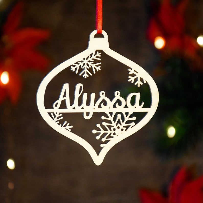 Op de afbeelding: Witte houten kerstversiering in de vorm van een traan met een sneeuwvlokkenontwerp en de naam "Alyssa" in cursief.