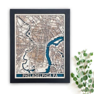 May include: A framed wooden map of Philadelphia, Pennsylvania, with a blue river and detailed street layout. The map is laser cut and has a black frame.
