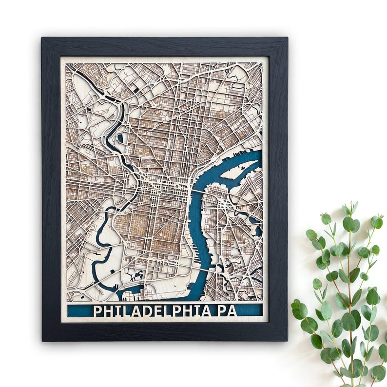 May include: A framed wooden map of Philadelphia, Pennsylvania, with a blue river and detailed street layout. The map is laser cut and has a black frame.