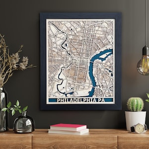 May include: A framed wooden map of Philadelphia, Pennsylvania with a blue background and the city name in white text. The map is detailed and shows the streets and waterways of the city.