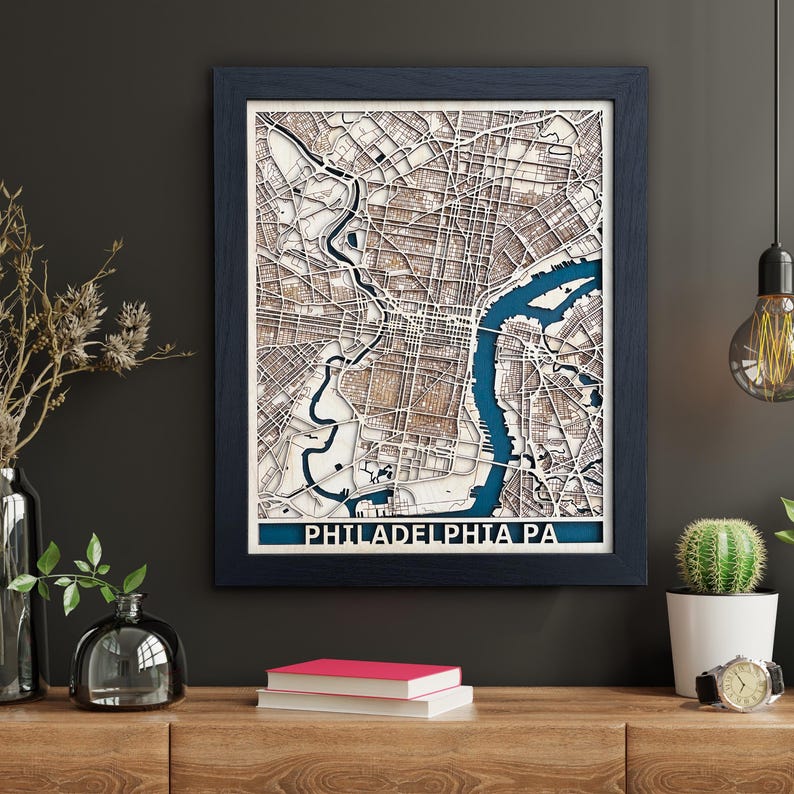 May include: A framed wooden map of Philadelphia, Pennsylvania with a blue background and the city name in white text. The map is detailed and shows the streets and waterways of the city.