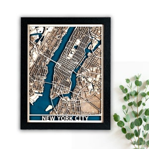 May include: A framed wooden map of New York City with a teal blue background. The map is raised and detailed, showing the streets and landmarks of the city. The frame is black and has a white mat.