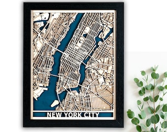 May include: A framed wooden map of New York City with a teal blue background. The map is raised and detailed, showing the streets and landmarks of the city. The frame is black and has a white mat.