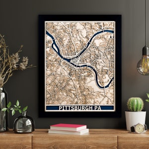 May include: A wooden wall art piece featuring a detailed map of Pittsburgh, Pennsylvania. The map is laser cut and painted in shades of brown and blue. The city name is displayed at the bottom of the map.