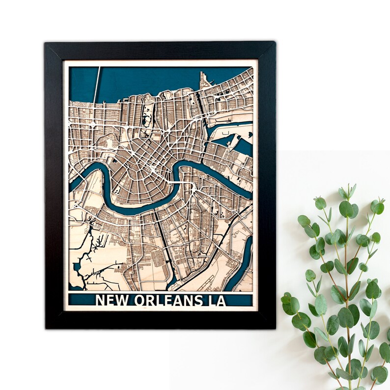 May include: A framed wooden map of New Orleans, LA, showing the city's layout and the Mississippi River in blue. The map is set against a teal background and framed in black. The city name is displayed at the bottom.