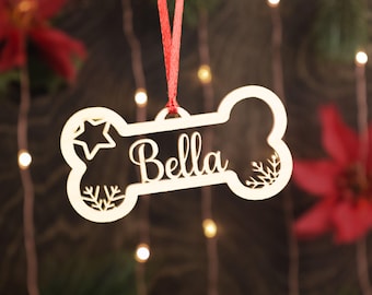 May include: A wooden dog bone Christmas ornament with the name "Bella" cut out. The ornament is hanging from a red ribbon and has a star and snowflake designs.