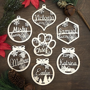 May include: Seven personalized wooden Christmas ornaments with snowflake designs. The ornaments feature the names "Victoria", "Misty", "Samuel", "Chief", "Matthew", "Katrina", and "Evalyn" with the year "2024" on each.