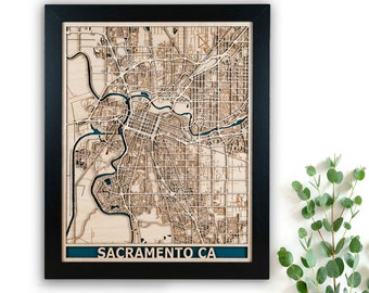 May include: A framed wooden map of Sacramento, California, with a blue border and the city name at the bottom. The map is detailed and shows the streets and waterways of the city.