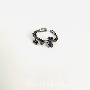 Peut inclure: Une délicate bague en argent avec un motif de vigne et de petites fleurs noires.