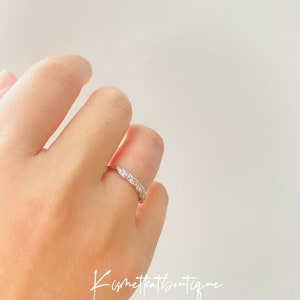 Op de afbeelding: Een zilveren ring met een rij kleine, heldere edelstenen. De ring zit om een vinger, tegen een witte achtergrond. Het ontwerp van de ring is een reeks kleine, sprankelende stenen. De tekst "Kismetkatboutique" is rechtsonder zichtbaar.