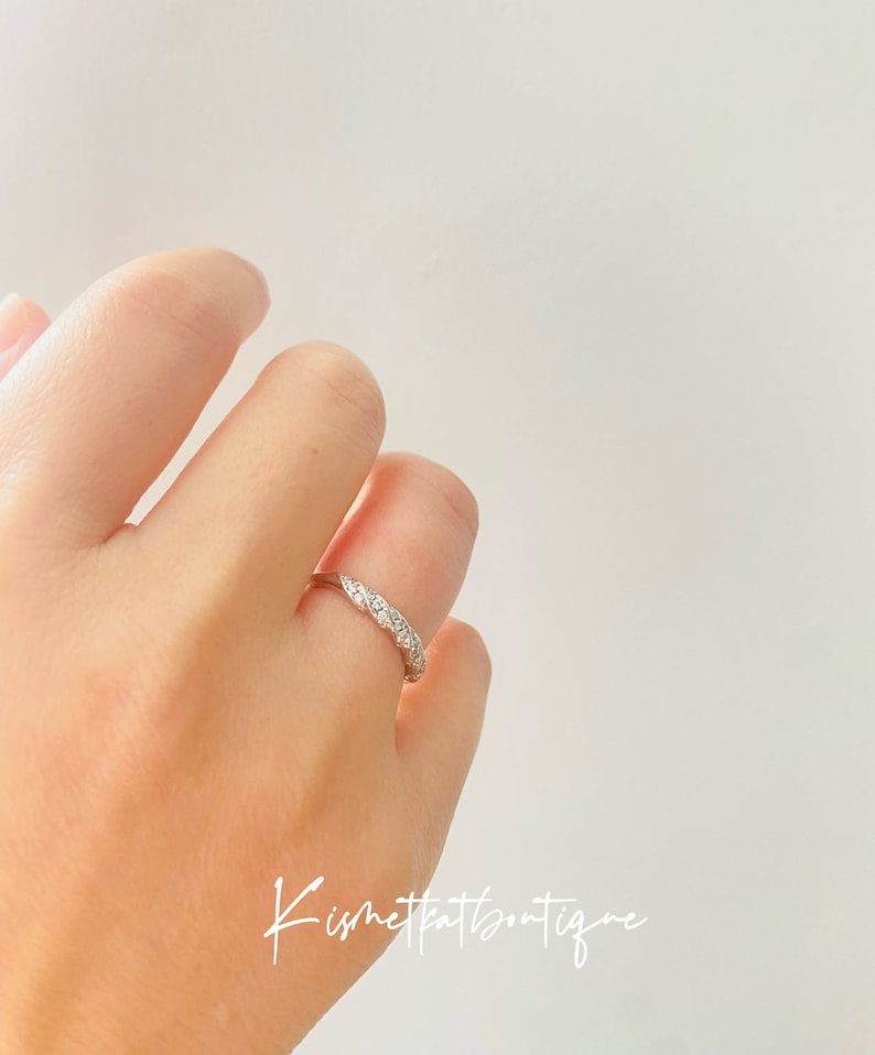 Op de afbeelding: Een zilveren ring met een rij kleine, heldere edelstenen. De ring zit om een vinger, tegen een witte achtergrond. Het ontwerp van de ring is een reeks kleine, sprankelende stenen. De tekst "Kismetkatboutique" is rechtsonder zichtbaar.