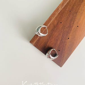 May include: A pair of silver hoop earrings with a unique, slightly curved design. The earrings are displayed on a wooden surface.