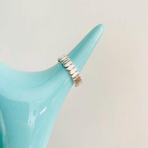 May include: A silver ring with a unique design featuring a series of connected oval-shaped links.