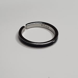 Pu&ograve; includere: Un anello d'argento con una fascia nera attorno al centro. L'anello ha il numero "925" inciso all'interno.