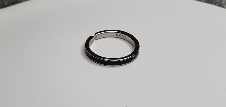 Pu&ograve; includere: Un anello d'argento con una fascia nera attorno al centro. L'anello ha il numero "925" inciso all'interno.