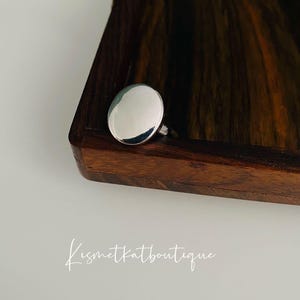 May include: A silver ring with a large, round, smooth top. The ring is sitting on a wooden surface.