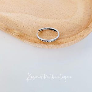 May include: A silver ring with a delicate design. The ring is on a wooden surface.