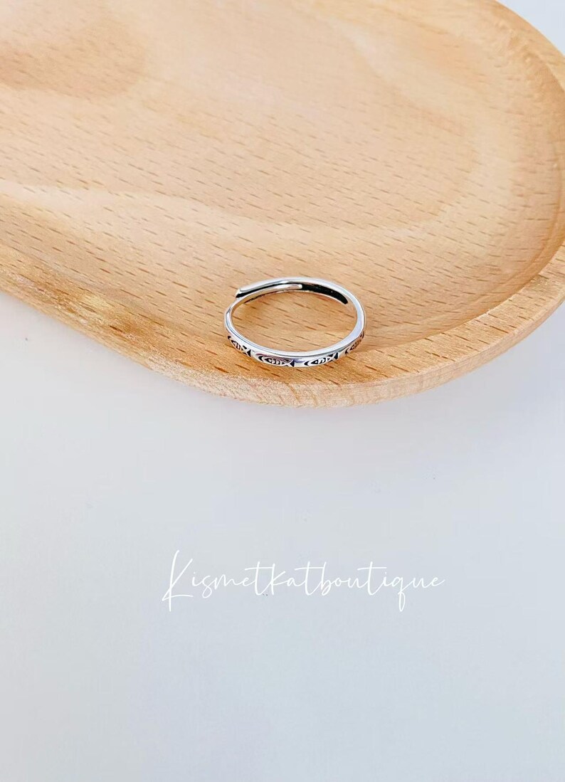 May include: A silver ring with a delicate design. The ring is on a wooden surface.