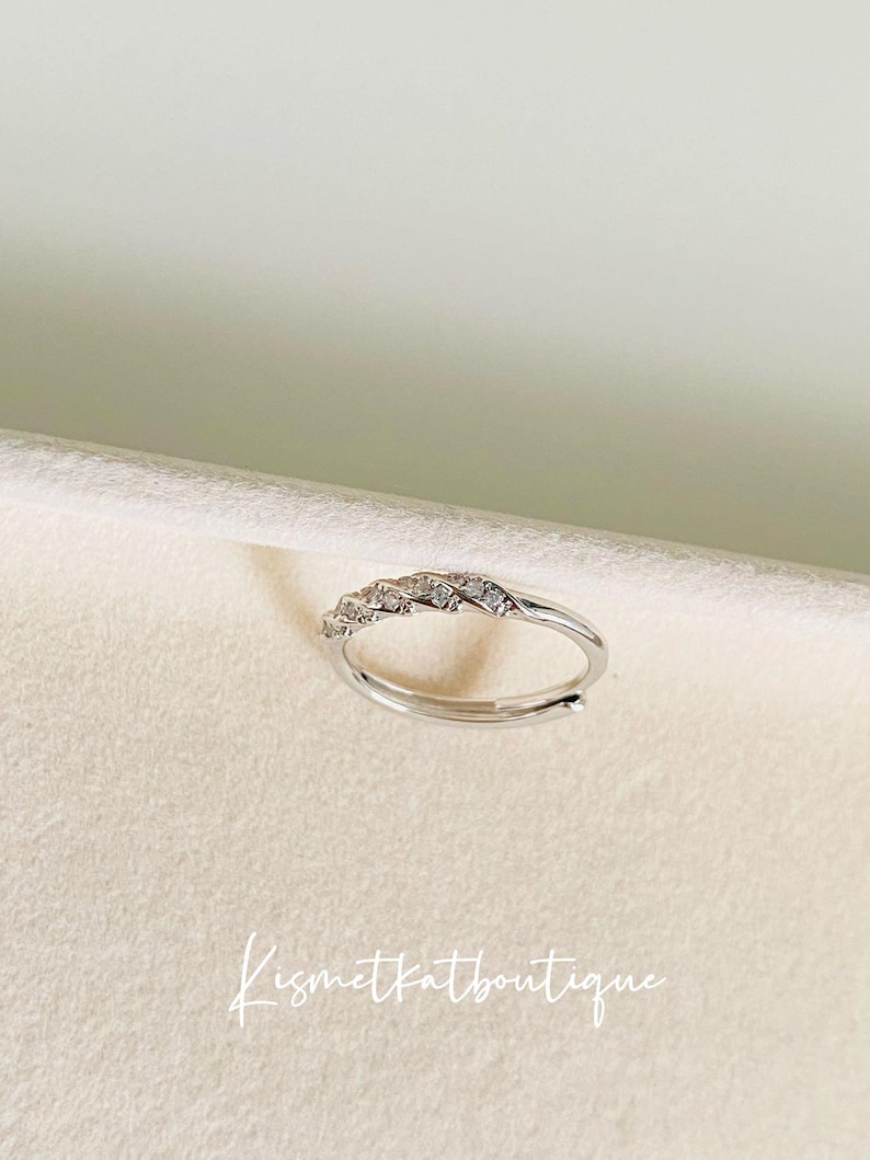 Op de afbeelding: Een verstelbare zilverkleurige ring met een rij kleine, heldere stenen. De ring wordt getoond op een neutrale achtergrond. De tekst "Kismetkatboutique" is zichtbaar in de afbeelding.