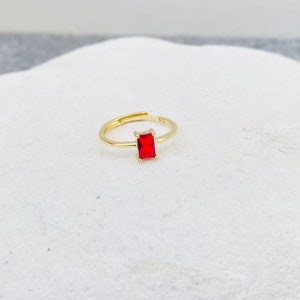 May include: A gold ring with a red rectangular gemstone.