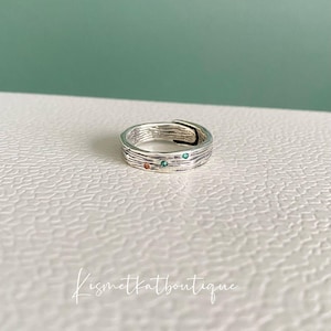 May include: A silver ring with a textured band and small green and red gemstones.