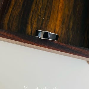 May include: A black and silver ring with a smooth, rounded surface. The ring is sitting on a wooden surface.