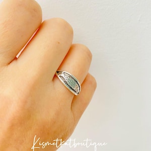 May include: A silver ring with a detailed fish design. The ring is worn on a person's finger.