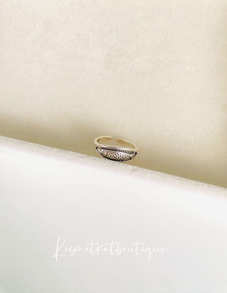 May include: Silver adjustable ring with a detailed fish design.